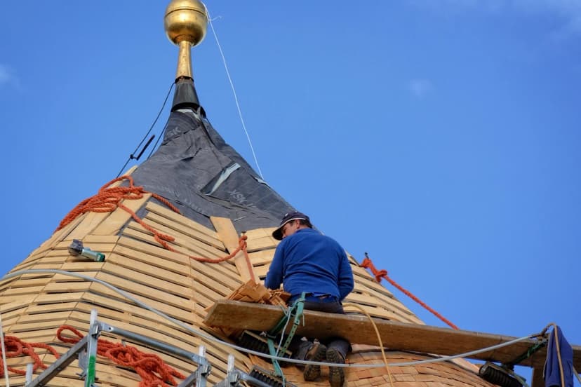 Roof restoration work on a spire against a blue sky