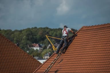 Roofer working on a sloped roof with safety gear.